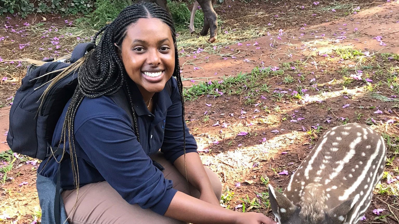 International Services employee outdoors, smiling and kneeling down next to a farm animal