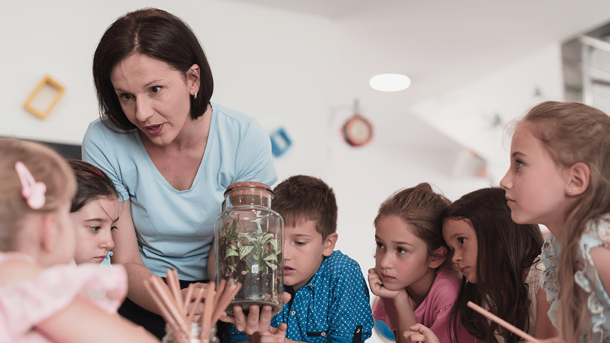 Female Teacher with kids in biology class at elementary school conducting biology or botanical scientific experiment about sustainable Growing plants. Learning about plants in a glass jar